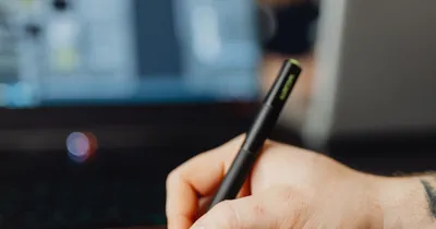 Mano sosteniendo un lápiz digital frente a un computador portátil, como metáfora de la firma digital de documentos