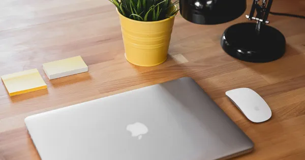 Computador Mac cerrado sobre un escritorio de madera, junto a un mouse de Apple y notas adhesivas