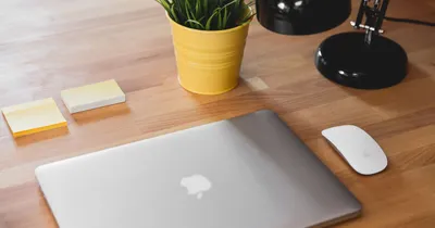 Computador Mac cerrado sobre un escritorio de madera, junto a un mouse de Apple y notas adhesivas