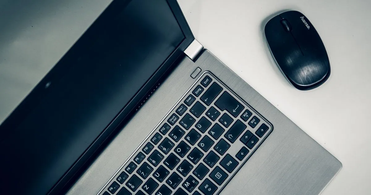 Portátil abierto con la pantalla apagada y un ratón inalámbrico sobre un escritorio blanco