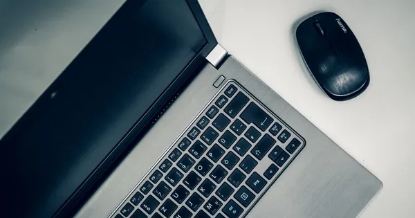 Portátil abierto con la pantalla apagada y un ratón inalámbrico sobre un escritorio blanco