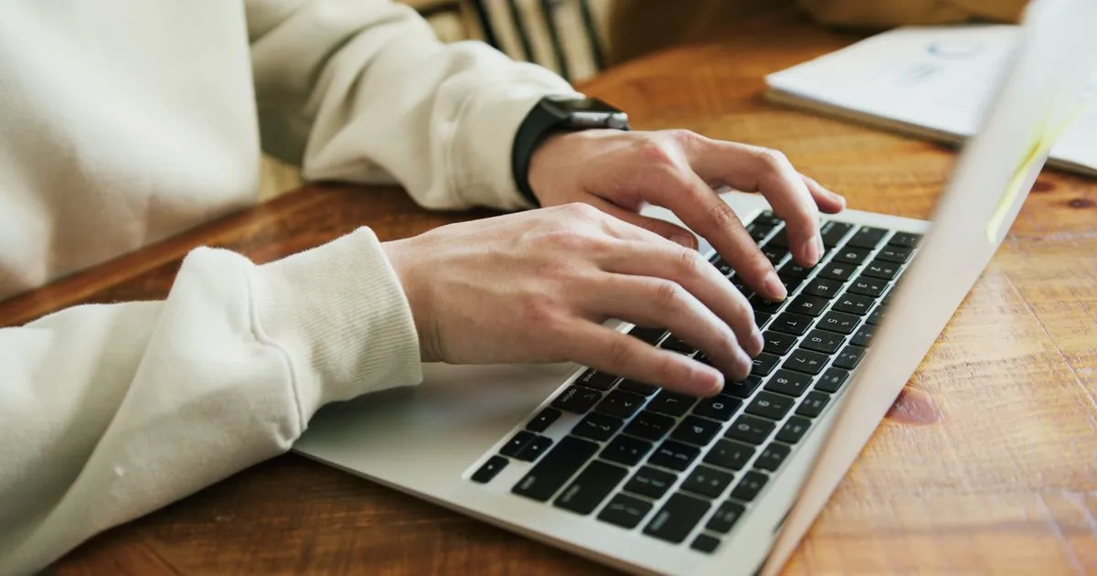 Manos escribiendo en el teclado de un portátil sobre una mesa de madera