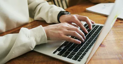 Manos escribiendo en el teclado de un portátil sobre una mesa de madera