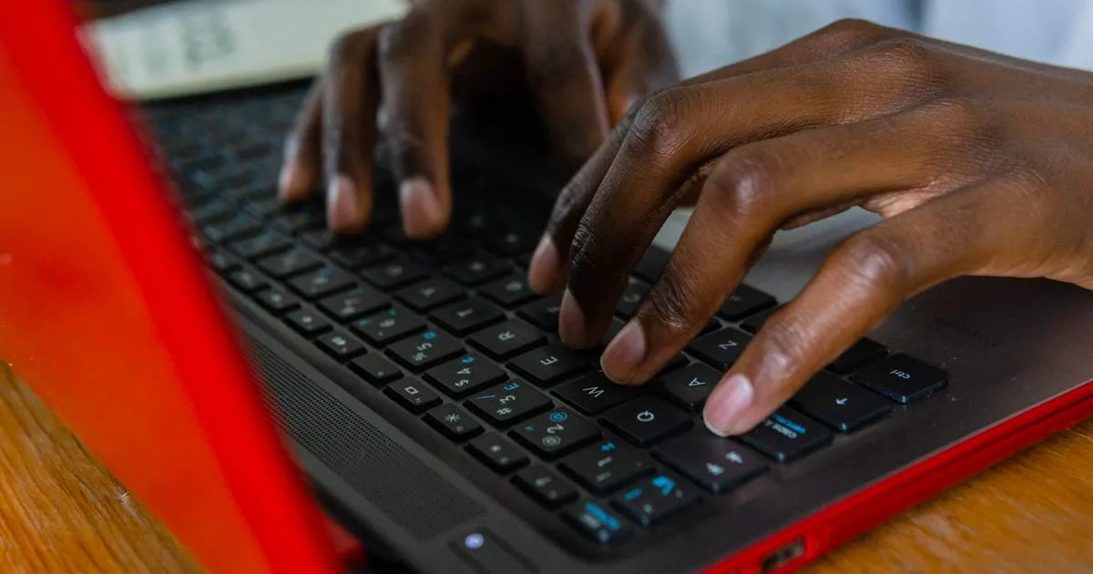 Manos tecleando sobre el teclado de un computador portátil rojo apoyado en un escritorio de madera