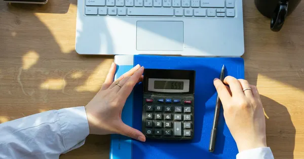 Vista cenital de un escritorio con calculadora, carpeta azul, lápiz y computador portátil