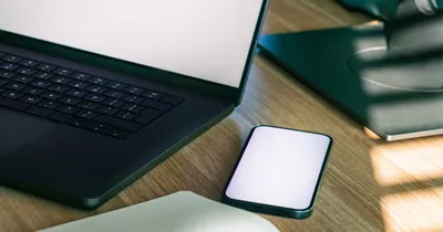 Teléfono con la pantalla en blanco junto a un computador portátil sobre un escritorio de madera
