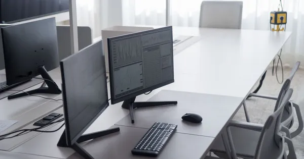 Puesto de trabajo de oficina con dos monitores y teclado, junto a una ventana