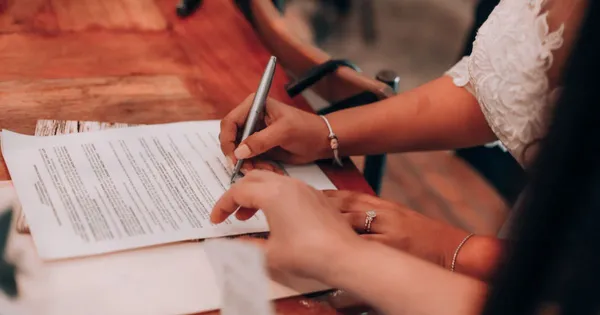 Dos personas firmando un documento en papel sobre una mesa de madera, vistas desde arriba