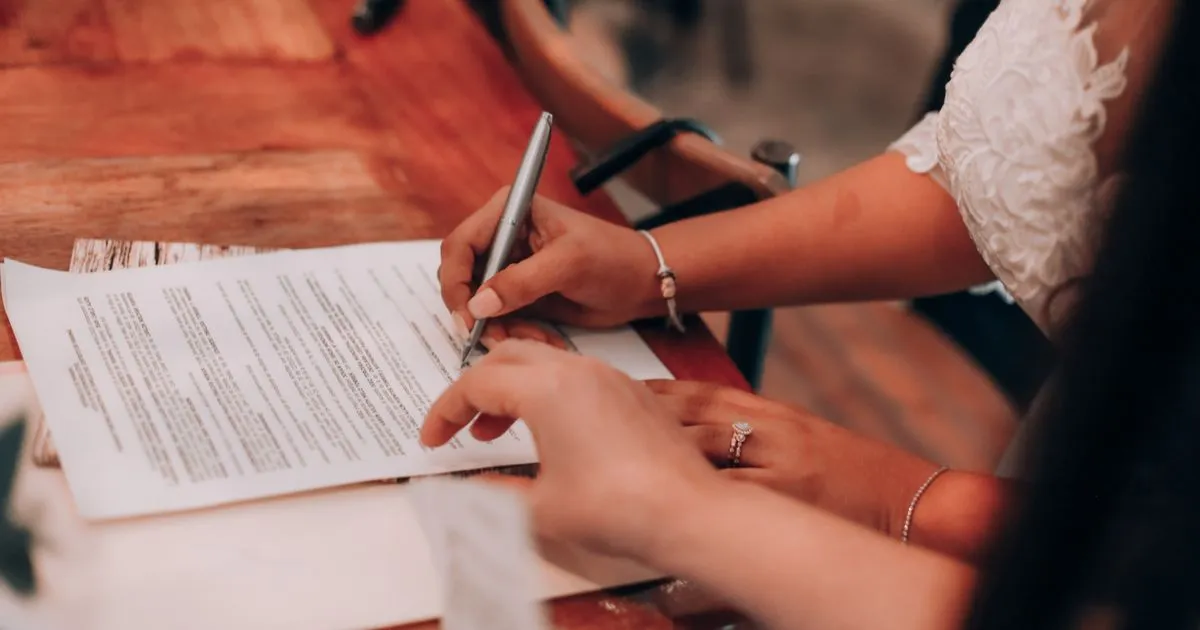 Dos personas firmando un documento en papel sobre una mesa de madera, vistas desde arriba