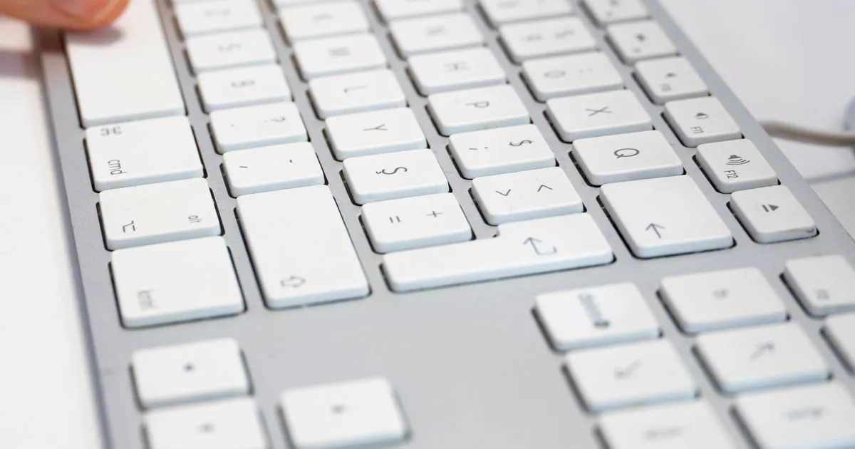 Primer plano de un teclado blanco de computador con luz natural, con un dedo a punto de pulsar una tecla