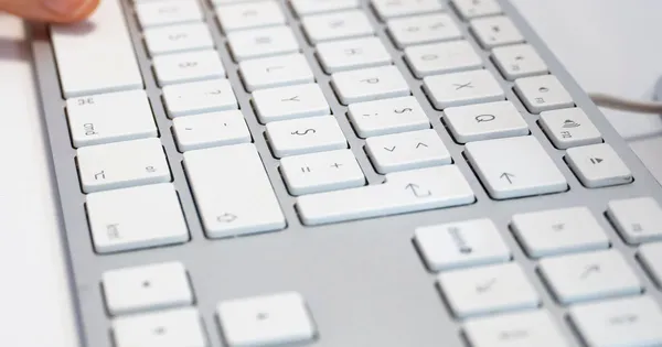 Primer plano de un teclado blanco de computador con luz natural, con un dedo a punto de pulsar una tecla