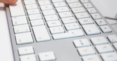 Primer plano de un teclado blanco de computador con luz natural, con un dedo a punto de pulsar una tecla