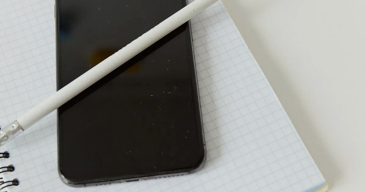 Teléfono móvil con la pantalla apagada sobre un cuaderno, junto a un lápiz